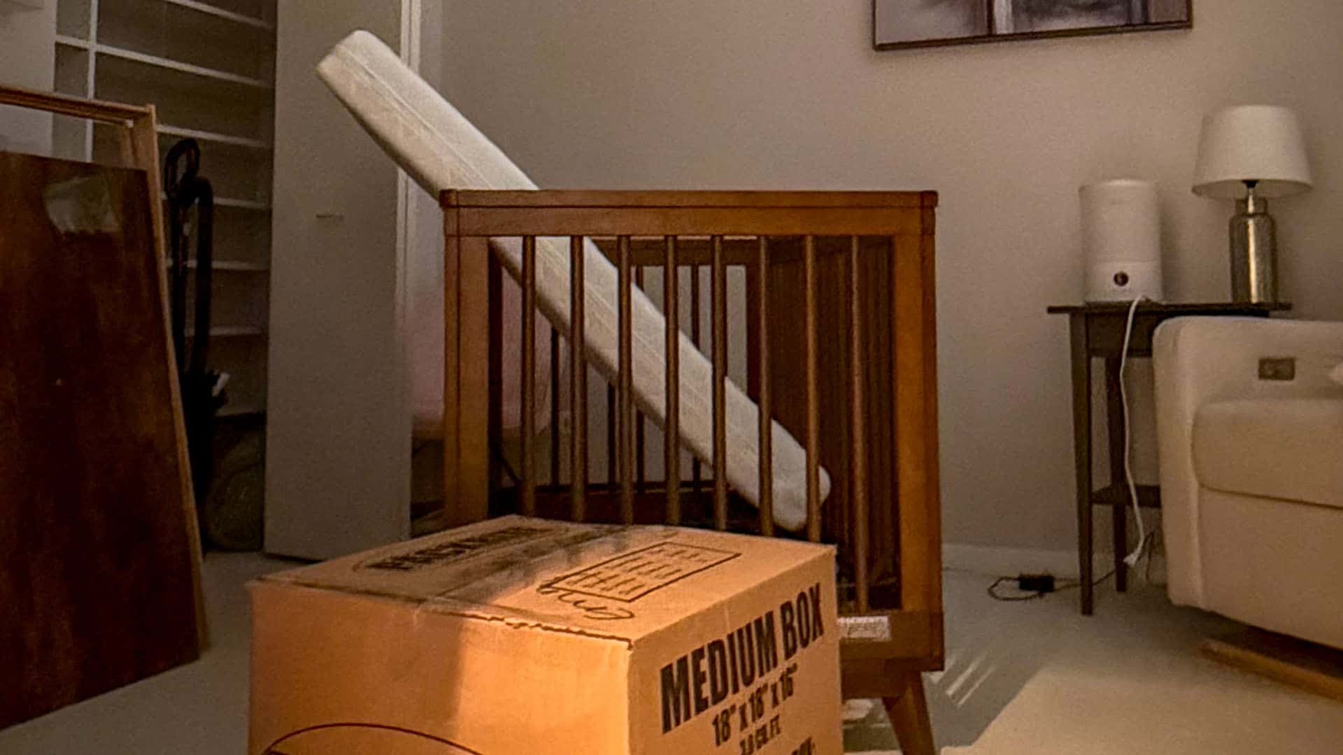 Crib with mattress and moving box in living room.