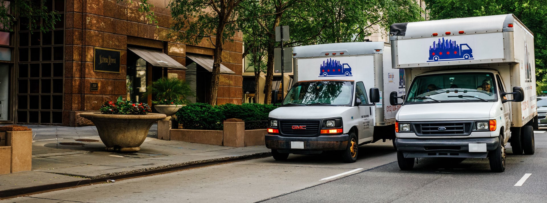 Moving trucks parked on city street near buildings.