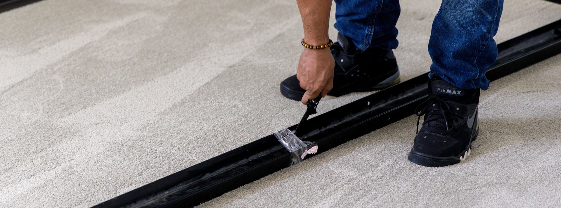Person cutting carpet with utility knife on floor.