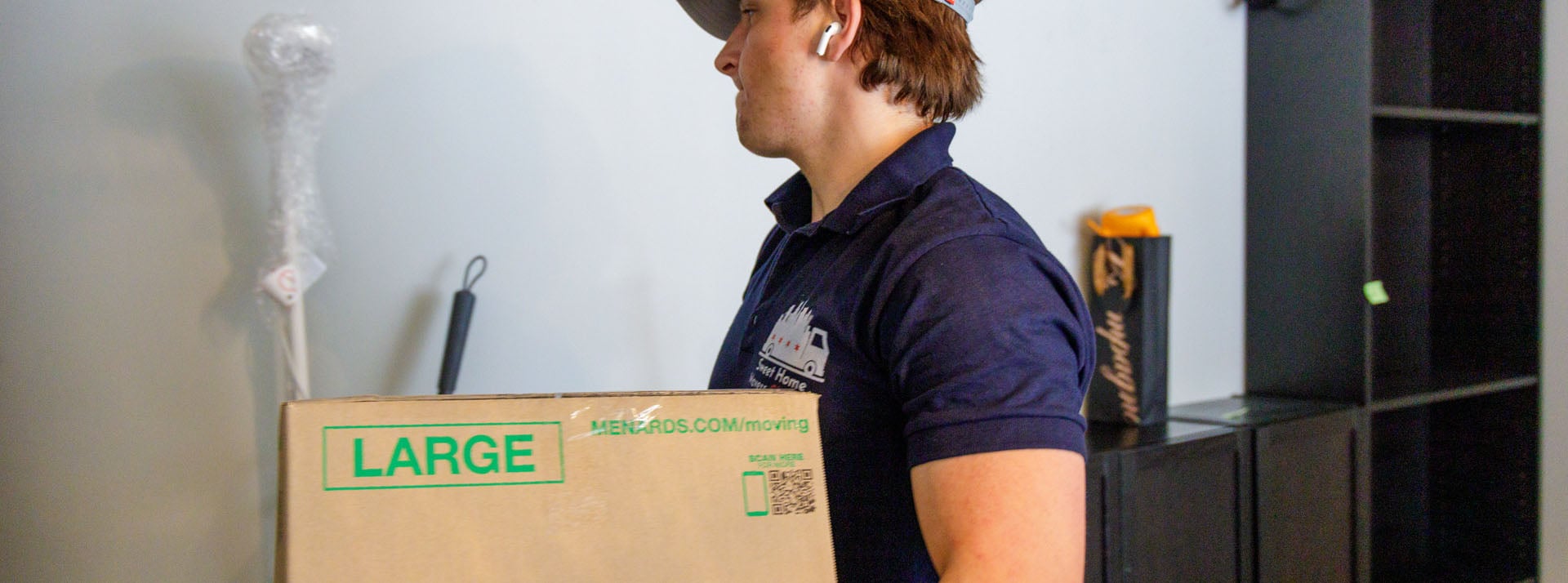 Person carrying large moving box indoors.
